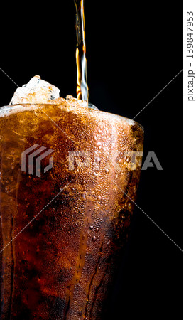 Soft drink pouring to glass with crushed ice cubes isolated on dark background with copy space. There is a drop of water on the transparent glass surface. Soft drink pouring to glass with crushed ice cubes isolated on dark background with copy space. There is a drop of water on the transparent glass surface. 139847953