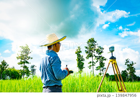 Asian smart engineer or surveyor working on controller screen for surveying land in rice field, Thailand. GPS surveying instrument. GPS equipment. Land survey for map. People work in good environment. Asian smart engineer or surveyor working on controller screen for surveying land in rice field, Thailand. GPS surveying instrument. GPS equipment. Land survey for map. People work in good environment. 139847956