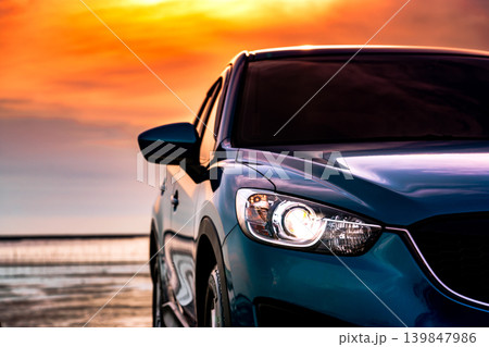 Blue compact SUV car with sport and modern design parked on the beach by the sea at sunset. Environmentally friendly technology. Business success concept. Front view car with open headlamp light. Blue compact SUV car with sport and modern design parked on the beach by the sea at sunset. Environmentally friendly technology. Business success concept. Front view car with open headlamp light. 139847986