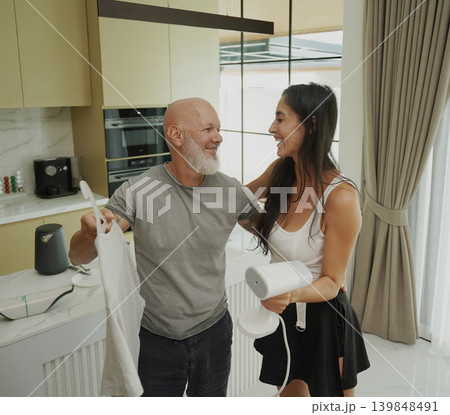 A couple ironing a t-shirt with a steam iron. A couple ironing a t-shirt with a steam iron. 139848491