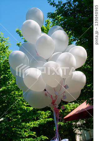 Cluster of White Balloons Floating Outdoors Over Green Trees and Bright Blue Sky 139848985