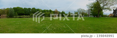 Wide Green Park Meadow With Trees And Lake Overlook Near Urban Residential Buildings In Spring 139848991