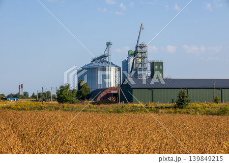Agricultural field shows grain silos and a storage building in a farmland setting under clear skies 139849215