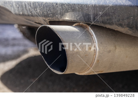 A car exhaust pipe shows exhaust gases coming out while the vehicle is parked on an unpaved road in the daytime A car exhaust pipe shows exhaust gases coming out while the vehicle is parked on an unpaved road in the daytime 139849228