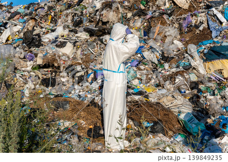 Environmentalist in white protective suit stands at a landfill site to study the effects of waste on the ecosystem and explore solutions Environmentalist in white protective suit stands at a landfill site to study the effects of waste on the ecosystem and explore solutions 139849235
