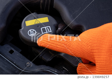 A mechanic uses a gloved hand to point at the antifreeze tank cap on a vehicle while performing maintenance in a garage 139849257