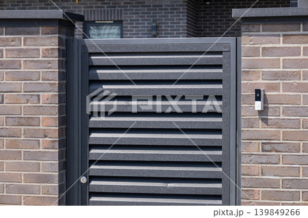 Modern gate stands at the entrance with intercom system installed on the wall. It provides access to a private residence Modern gate stands at the entrance with intercom system installed on the wall. It provides access to a private residence 139849266