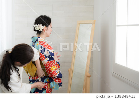 鏡で浴衣姿を確認する日本人女性の着付け準備をする人と浴衣の女性イメージ　お端折りの調整 139849413