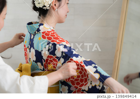 鏡で浴衣姿を確認する日本人女性の着付け準備をする人と浴衣の女性イメージ 顔無しの後姿 鏡で浴衣姿を確認する日本人女性の着付け準備をする人と浴衣の女性イメージ 顔無しの後姿 139849414