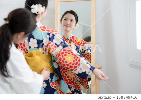 鏡で浴衣姿を確認する日本人女性の着付け準備をする人と浴衣の女性イメージ 鏡で浴衣姿を確認する日本人女性の着付け準備をする人と浴衣の女性イメージ 139849416