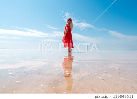 A woman wearing a flowing red dress and long, colorful dreadlocks walks into the shimmering shallow waters of Bursol lake A woman wearing a flowing red dress and long, colorful dreadlocks walks into the shimmering shallow waters of Bursol lake 139849511