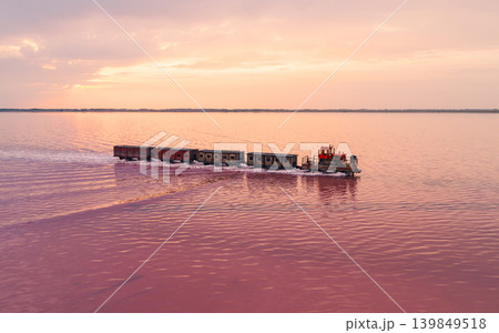 Aerial view captures specialized locomotive pulls several wagons across the strikingly pink waters of Bursol Lake Aerial view captures specialized locomotive pulls several wagons across the strikingly pink waters of Bursol Lake 139849518