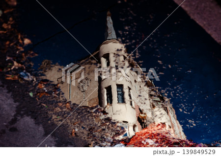 A striking reflection of a unique, old urban building in a puddle after rain Moody high-contrast image captures architectural details and the sky in the water's surface, highlighted by a splash of red A striking reflection of a unique, old urban building in a puddle after rain Moody high-contrast image captures architectural details and the sky in the water's surface, highlighted by a splash of red 139849529