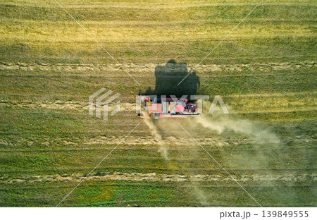 A powerful combine harvester cuts and processes crops in a wide green field, creating a large dust cloud. A powerful combine harvester cuts and processes crops in a wide green field, creating a large dust cloud. 139849555