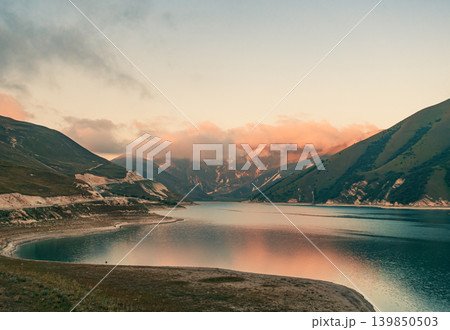 Peaceful waters of Lake Kazenoy-Am reflecting soft evening light on surrounding mountains at sunset Peaceful waters of Lake Kazenoy-Am reflecting soft evening light on surrounding mountains at sunset 139850503