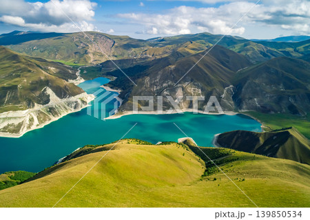 Panoramic view capturing Lake Kazenoy's striking turquoise waters contrasting with steep, sun-kissed mountains under bright blue sky 139850534