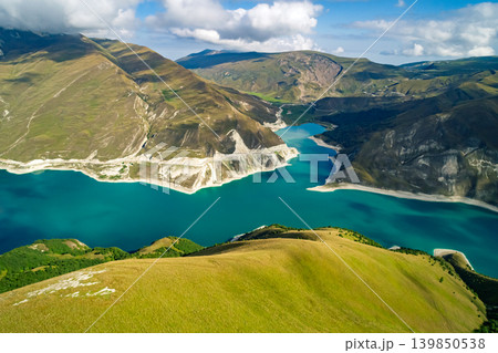 Panoramic view capturing Lake Kazenoy's striking turquoise waters contrasting with steep, sun-kissed mountains under bright blue sky 139850538