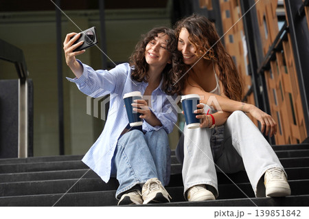 Two young women drink coffee and take pictures near the entrance to the office. 139851842