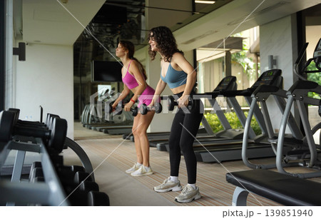 Two women sharing dumbbell workout with spotting assistance Two women sharing dumbbell workout with spotting assistance 139851940