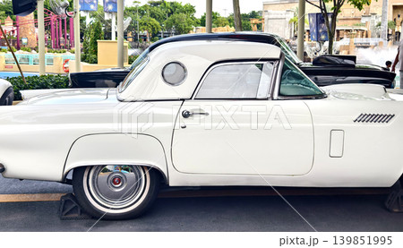 White classic car parked on street, gleaming chrome trim and polished hubcap reflecting sunny urban 139851995