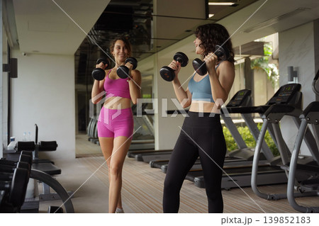 Two women sharing dumbbell workout with spotting assistance 139852183