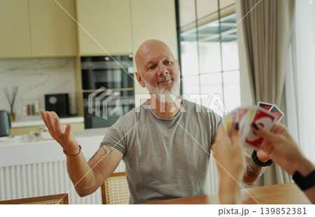 A man and a woman play cards at a wooden table in a sunlit modern living room A man and a woman play cards at a wooden table in a sunlit modern living room 139852381