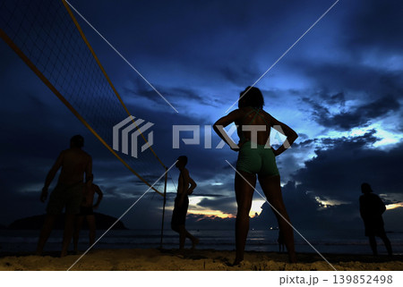 Young people playing beach volleyball by the ocean at sunset 139852498