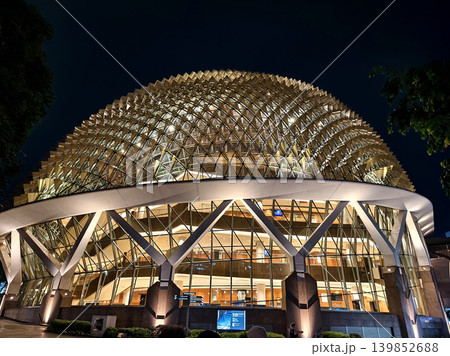 Modern illuminated dome with glass entrance, City skyline frames luminous theater at night 139852688
