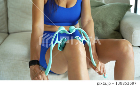 A woman in blue workout clothes uses a turquoise roller to thigh 139852697