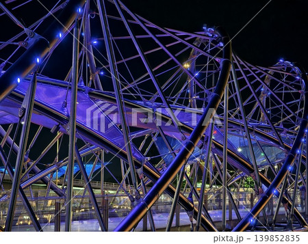 Modern illuminated helix bridge adorned with colorful lights over tranquil waterfront scene 139852835