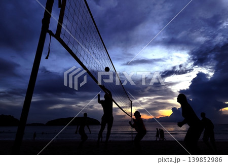 Young people playing beach volleyball by the ocean at sunset Young people playing beach volleyball by the ocean at sunset 139852986