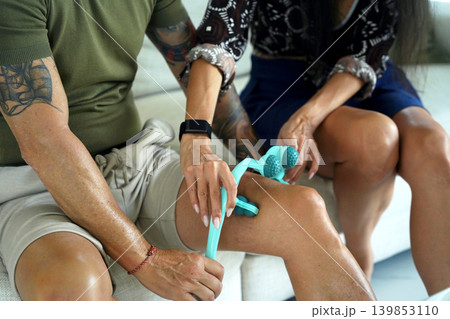 A woman helps a man use a massage roller to rehabilitate his knee 139853110