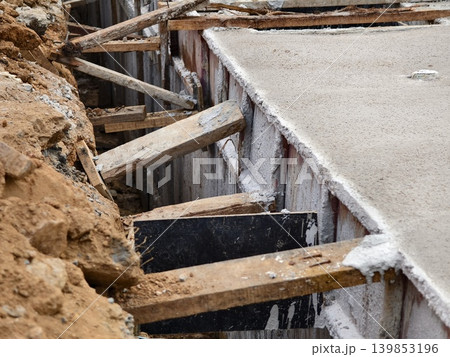 Narrow ditch with reinforcement, waterproof concrete trench bounded by soil and support stakes Narrow ditch with reinforcement, waterproof concrete trench bounded by soil and support stakes 139853196