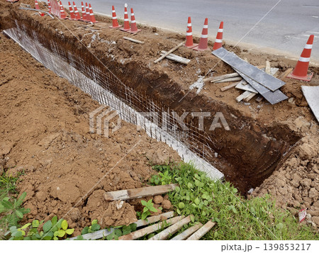 Narrow ditch with reinforcement, waterproof concrete trench bounded by soil and support stakes 139853217