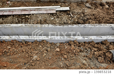 Narrow ditch with reinforcement, waterproof concrete trench bounded by soil and support stakes Narrow ditch with reinforcement, waterproof concrete trench bounded by soil and support stakes 139853218