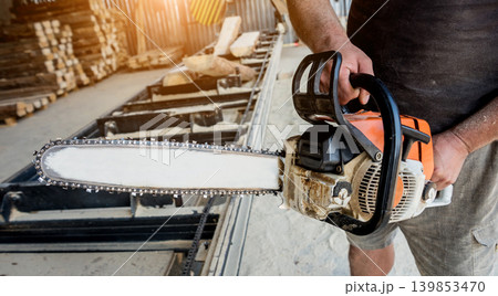 Woodcutter cutting tree with chainsaw on sawmill. Modern sawmill. 139853470