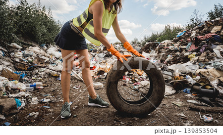 Woman volunteer helps clean the field of plastic garbage and old tires. Woman volunteer helps clean the field of plastic garbage and old tires. 139853504