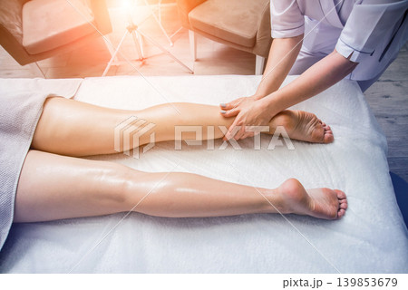 Beautiful young woman enjoying legs massage with oil in spa salon. Cosmetology Beautiful young woman enjoying legs massage with oil in spa salon. Cosmetology 139853679