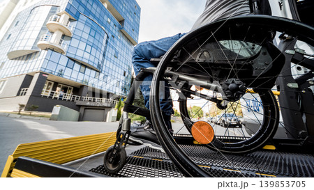 A man in a wheelchair on a lift of a vehicle for people with disabilities A man in a wheelchair on a lift of a vehicle for people with disabilities 139853705