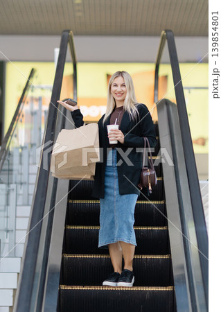 Smiling woman holding shopping bags on escalator lifestyle Smiling woman holding shopping bags on escalator lifestyle 139854801