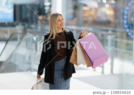Woman holding shopping bags pointing in mall Woman holding shopping bags pointing in mall 139854810