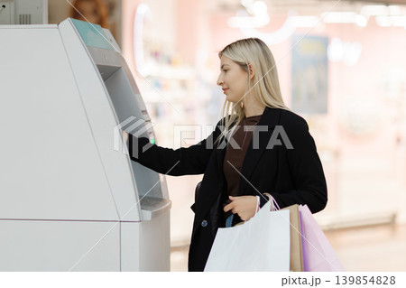 Young woman withdrawing cash from ATM after shopping 139854828