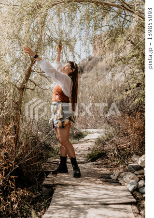 Woman willow nature young woman stands on a wooden path reaching for tree branches in a sunny park landscape 139855093