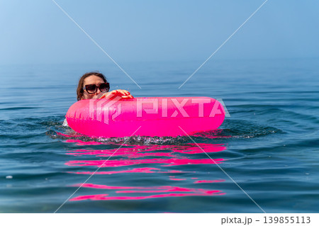 Woman floating pink inflatable ring, swimming in deep blue ocean water during a sunny summer vacation holiday Woman floating pink inflatable ring, swimming in deep blue ocean water during a sunny summer vacation holiday 139855113