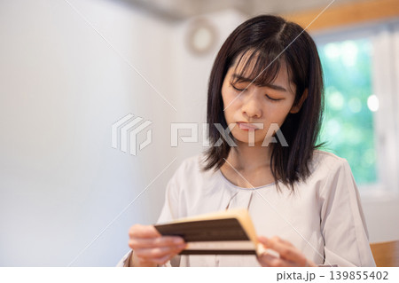 通帳を見て顔をしかめる日本人の若い女性 通帳を見て顔をしかめる日本人の若い女性 139855402