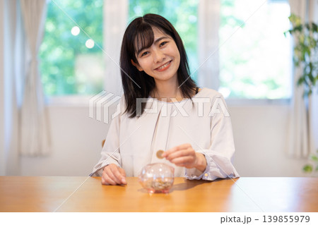 豚の貯金箱に硬貨を入れながら微笑む日本人の若い女性 豚の貯金箱に硬貨を入れながら微笑む日本人の若い女性 139855979
