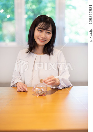 豚の貯金箱に硬貨を入れながら微笑む日本人の若い女性 139855981