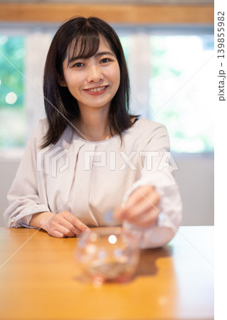 豚の貯金箱に硬貨を入れながら微笑む日本人の若い女性 豚の貯金箱に硬貨を入れながら微笑む日本人の若い女性 139855982