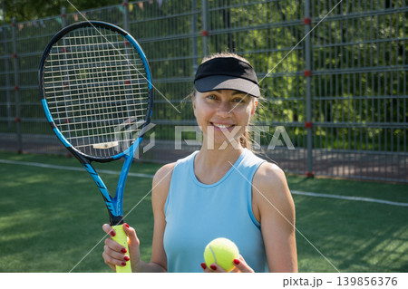 Female tennis player with racket and ball on green outdoor court 139856376