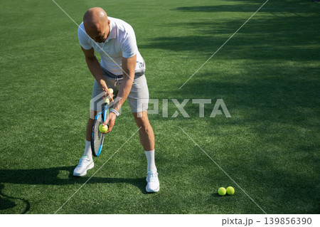 Athletic mature tennis player standing with racket and ball outdoors Athletic mature tennis player standing with racket and ball outdoors 139856390